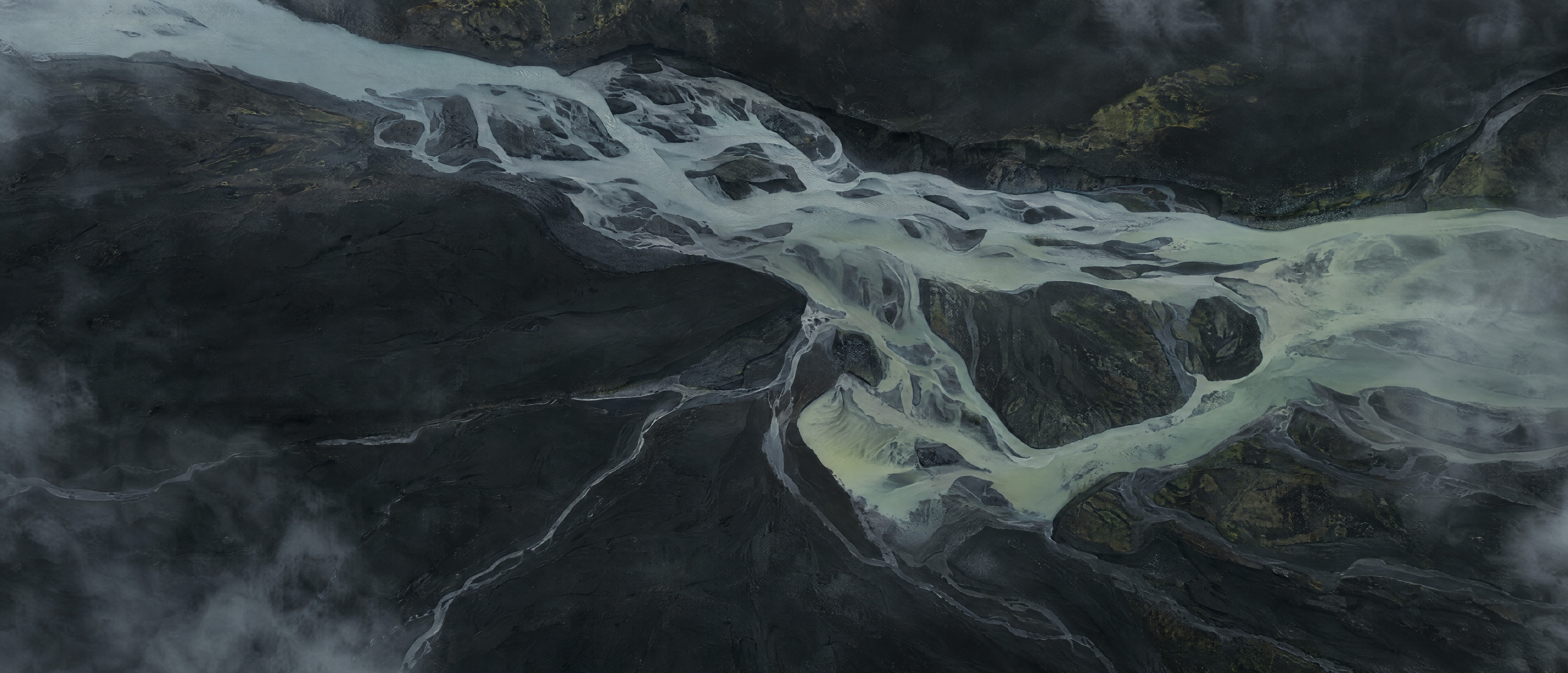 A braided glacial river seen from above, splitting and rejoining across black sand